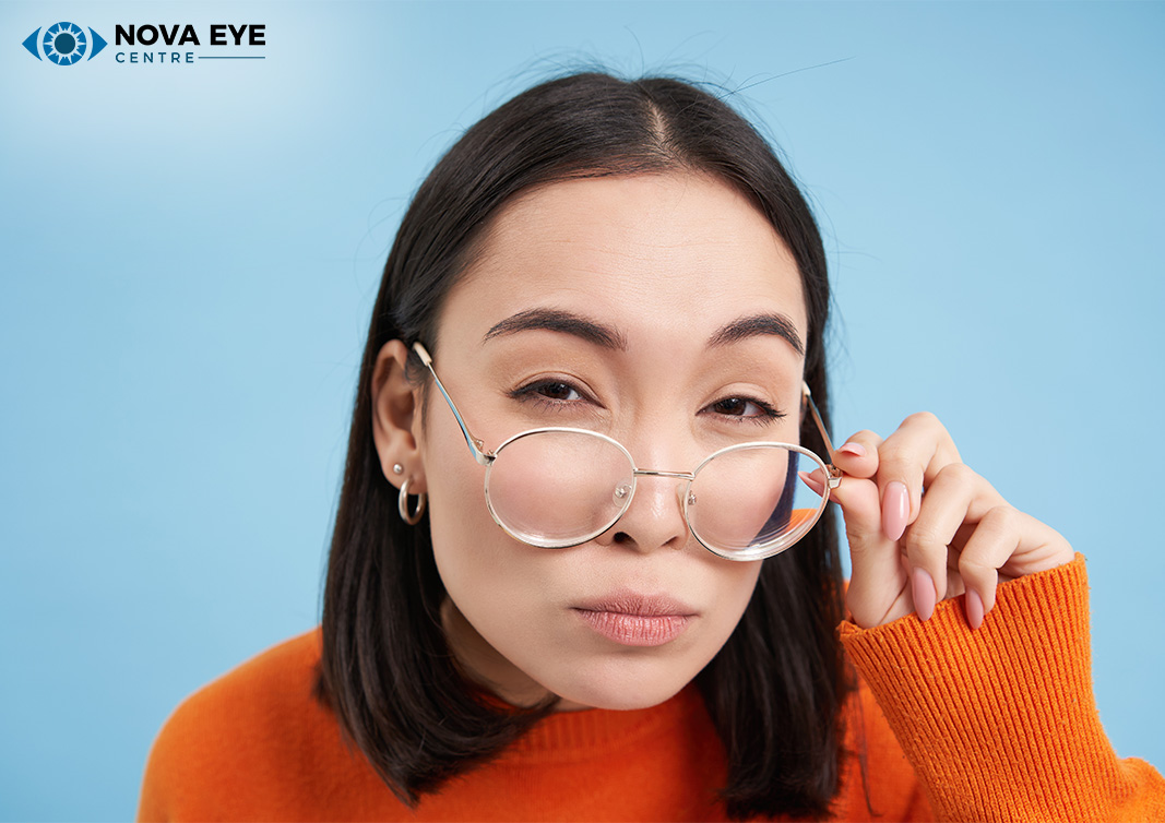 A woman with dark hair and glasses looking over the top of her frames against a blue background