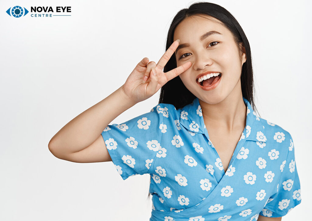 A young woman in a floral shirt smiling and holding up a peace sign over her eye.